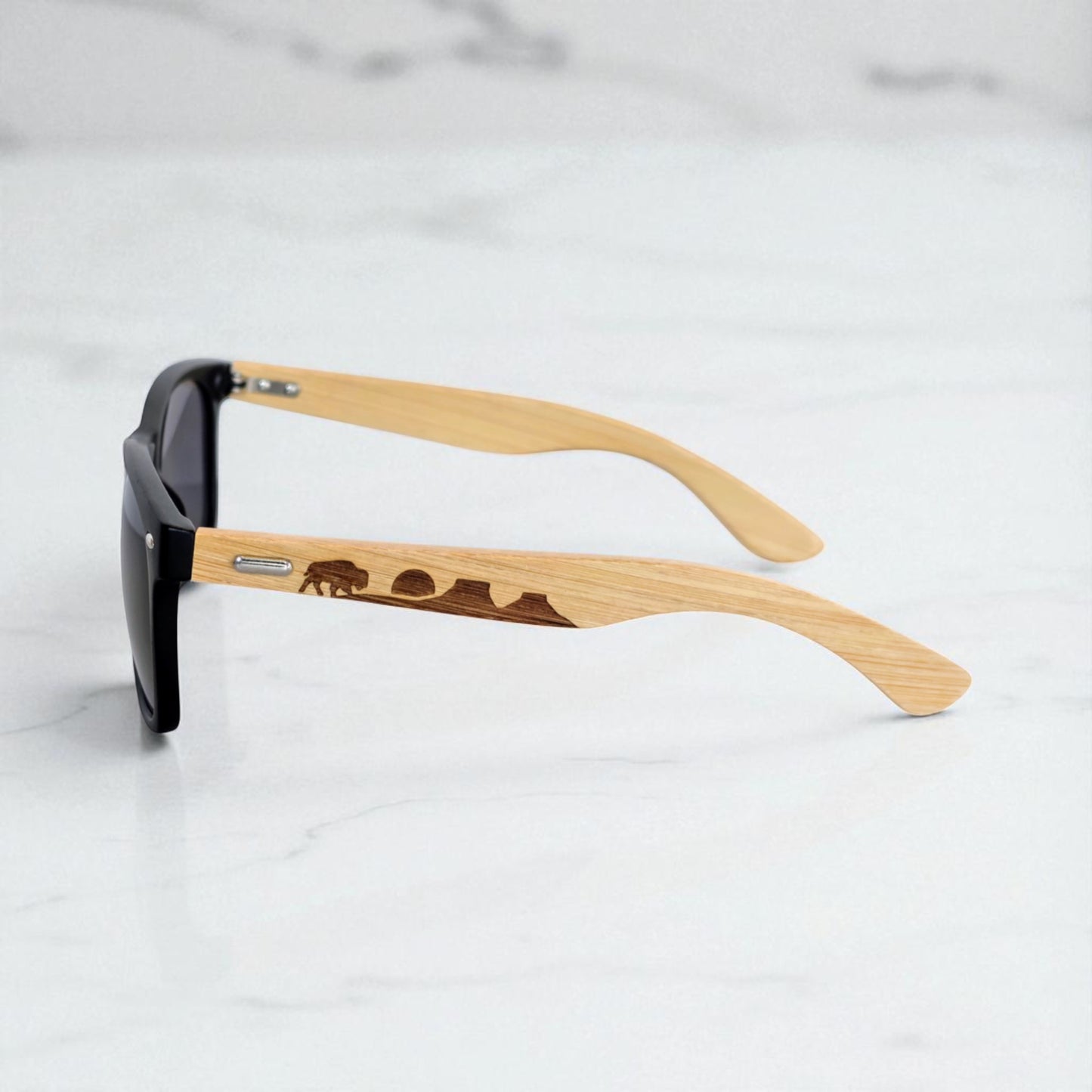Side profile view of eco-friendly bamboo sunglasses featuring a bison, setting sun, and mountain range etched into the arms. Designed for outdoor enthusiasts in Oklahoma, these sunglasses combine comfort, craftsmanship, and state pride in a modern, adventure-ready look.