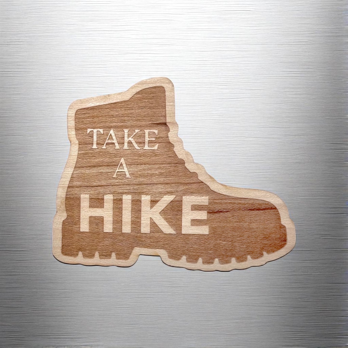 “Take a Hike” hiking boot wood sticker applied to a brushed metal water bottle or laptop, showing natural wood grain detail
