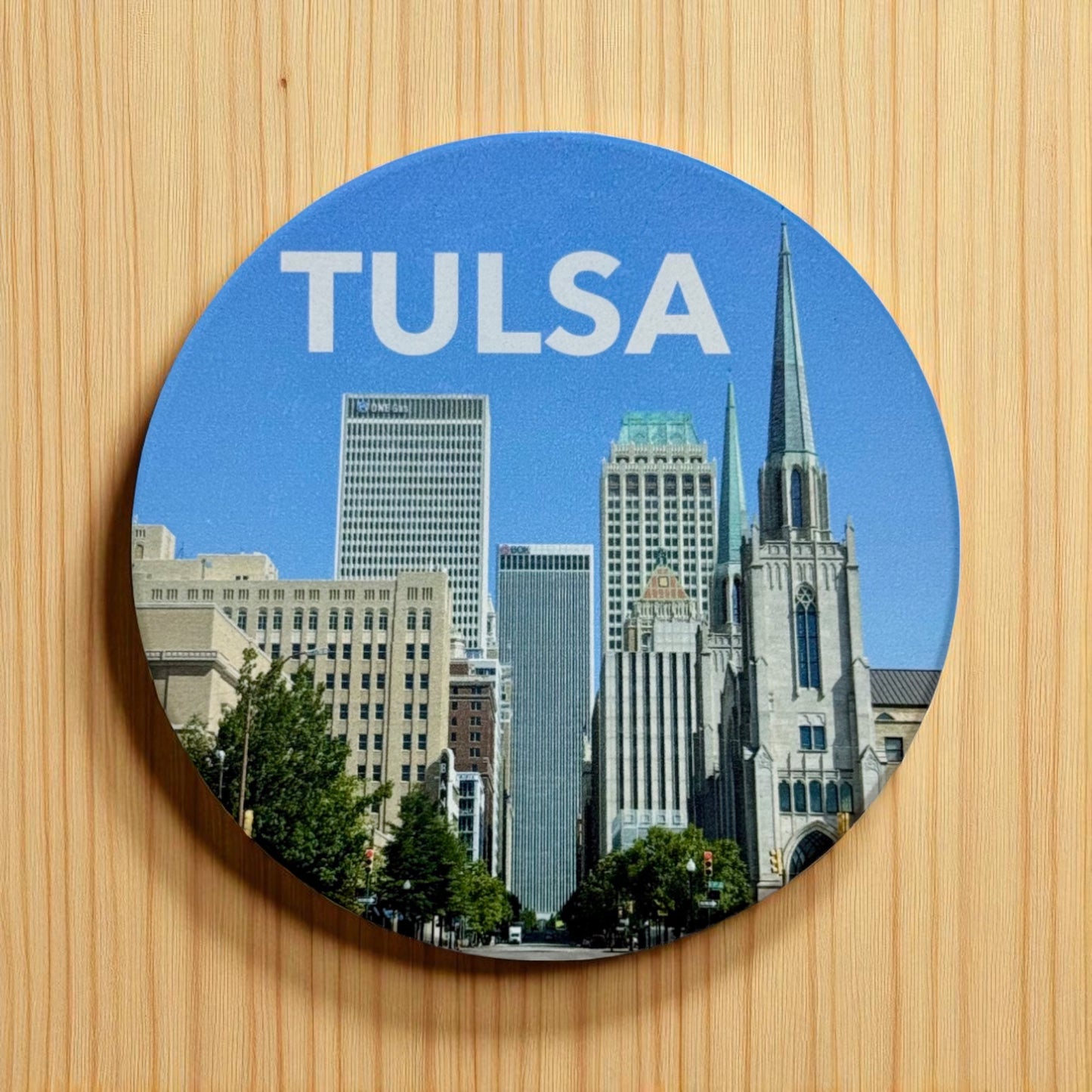 Round ceramic coaster featuring Tulsa skyline from Boston Avenue with downtown buildings and church spires on a bright blue day