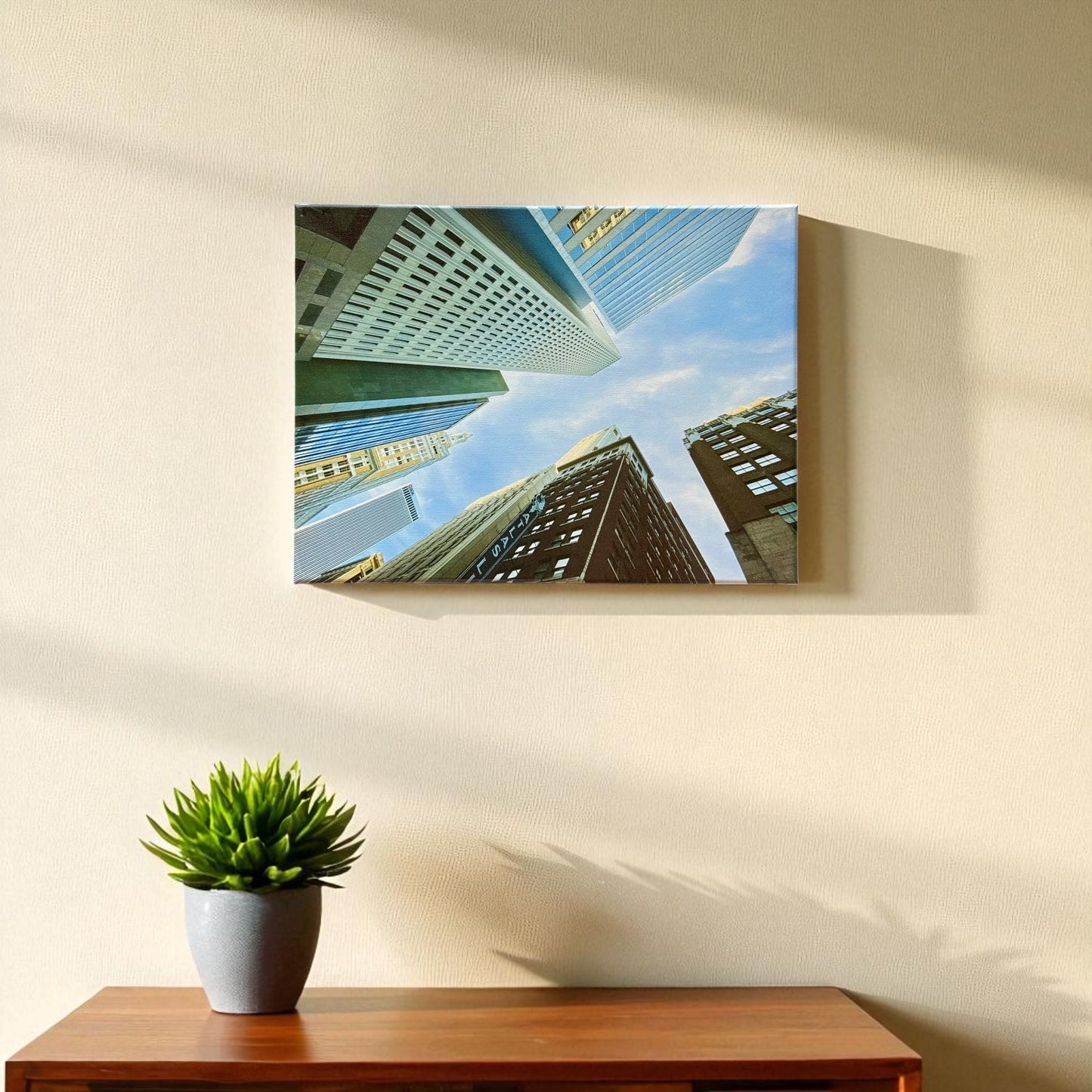 12x16 inch canvas of Tulsa downtown buildings hanging on a beige wall above a wooden table with a small potted succulent, lit by natural sunlight