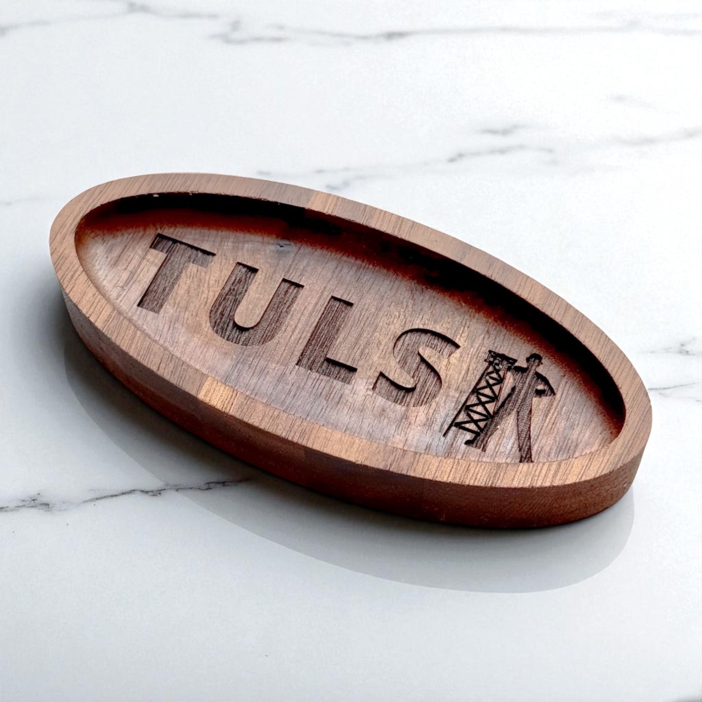 Angled view of an oval walnut catchall tray with engraved Tulsa lettering and driller symbol, shown on marble surface