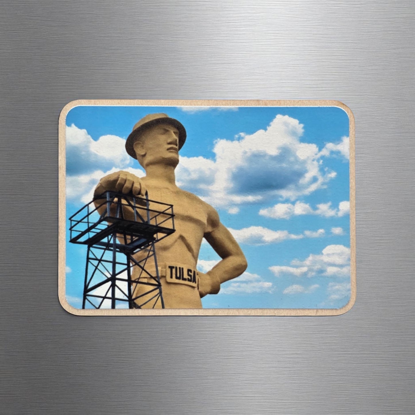 Tulsa Golden Driller wood magnet on a brushed metal surface. The magnet shows the massive Oklahoma landmark under a bright sky, highlighting the state’s oil history and Route 66 charm.