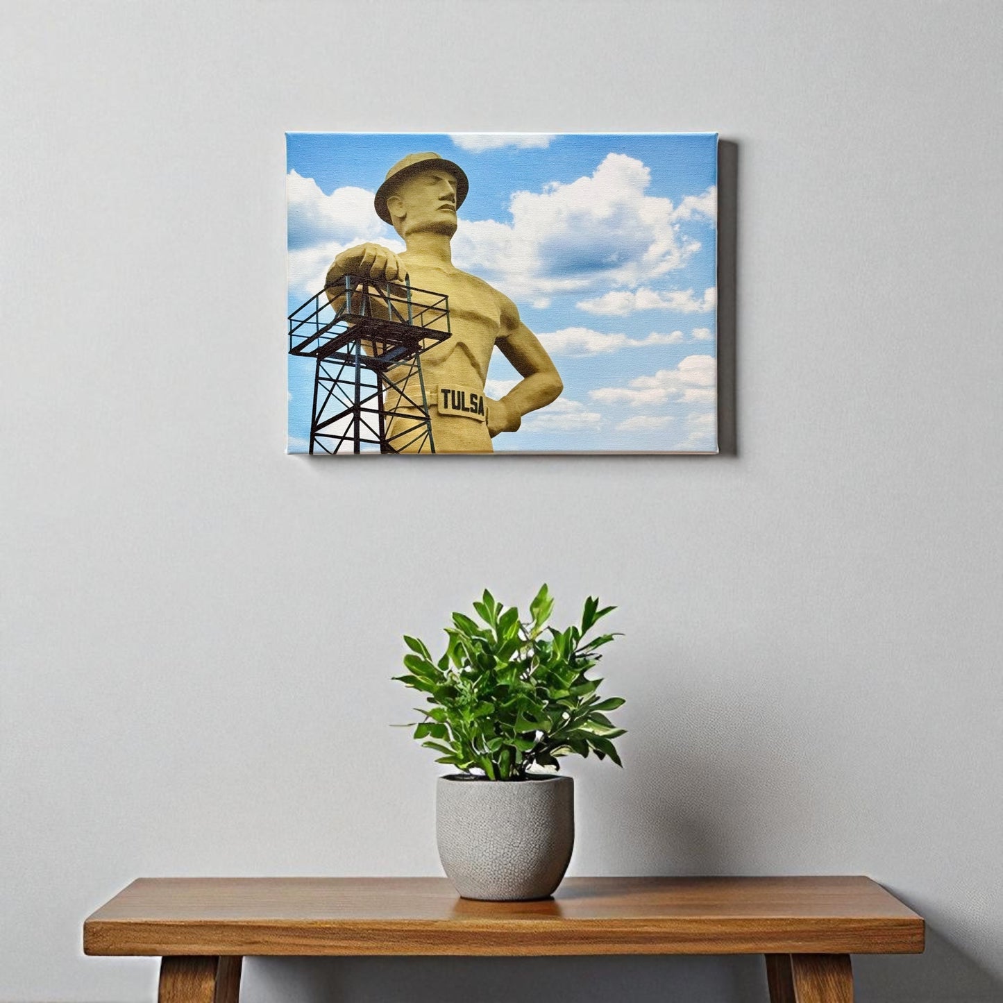 12x16 Tulsa Golden Driller canvas wall art displayed on a neutral gray wall above a wooden bench, with a modern potted plant underneath.