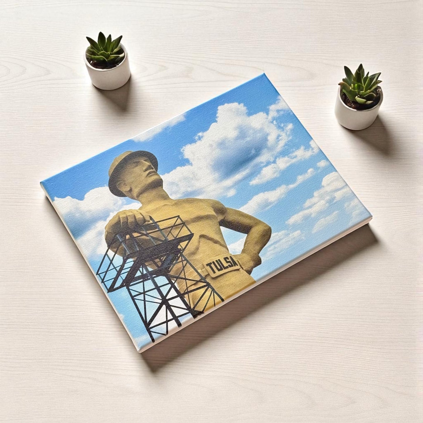 Flat-lay view of Tulsa Golden Driller 12x16 canvas print on a light wood surface, styled with mini succulents for a clean and modern look.