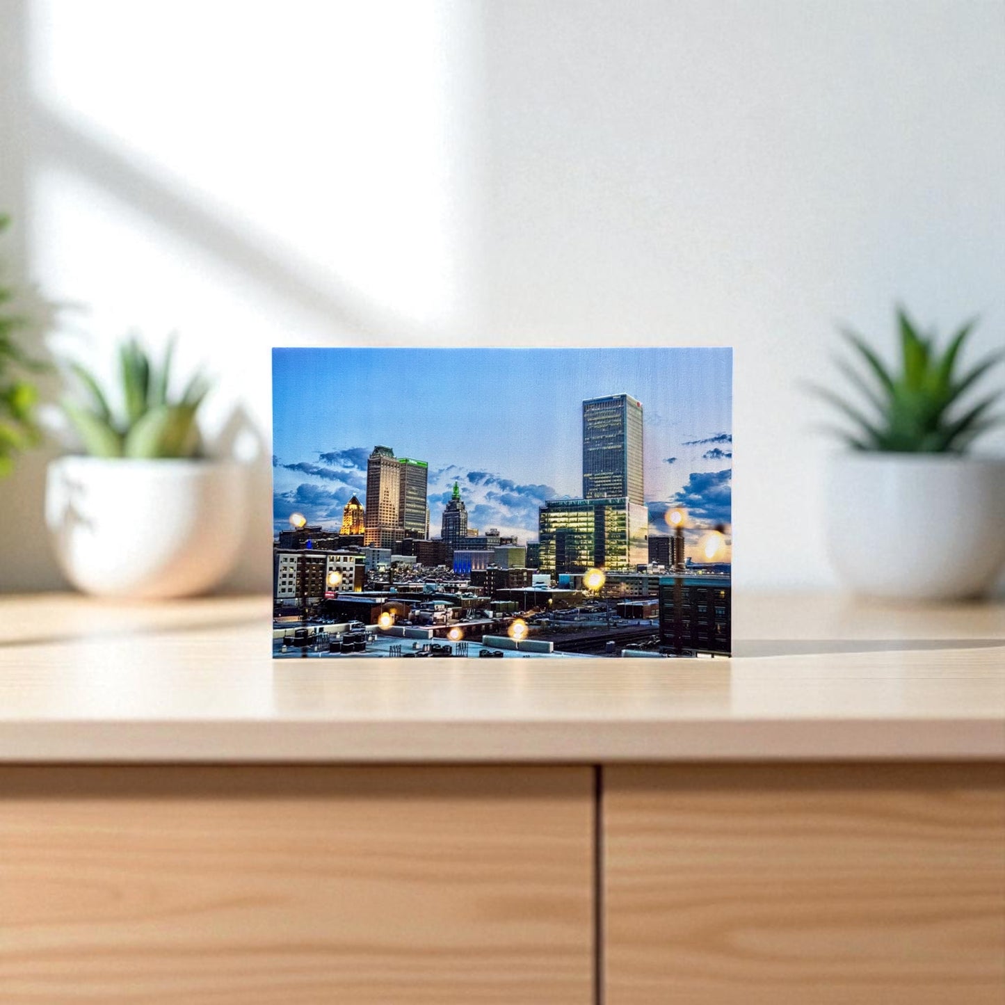 Cityscape on a glass panel with plants on either side on a wooden surface
