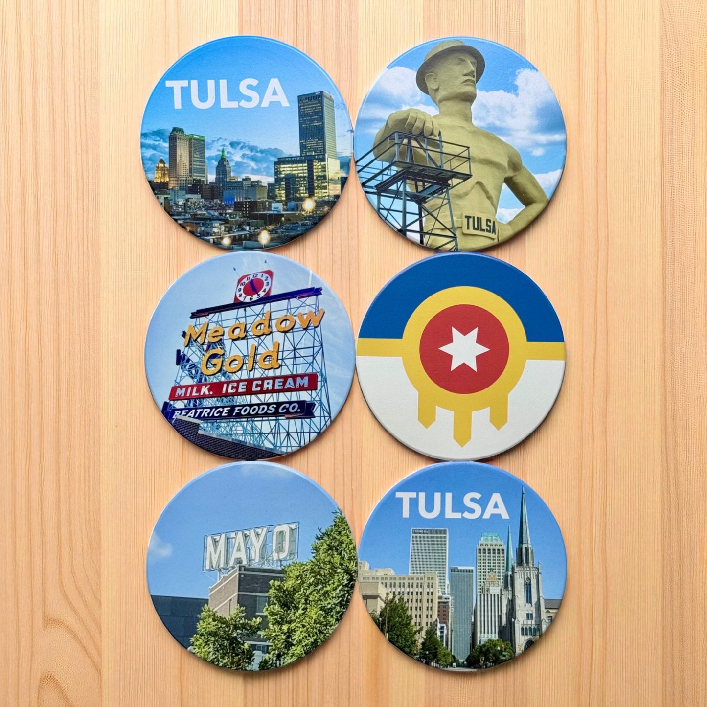 Set of Tulsa photo ceramic coasters laid out on wood surface featuring local landmarks including Golden Driller, Meadow Gold sign, Tulsa flag, and skyline views