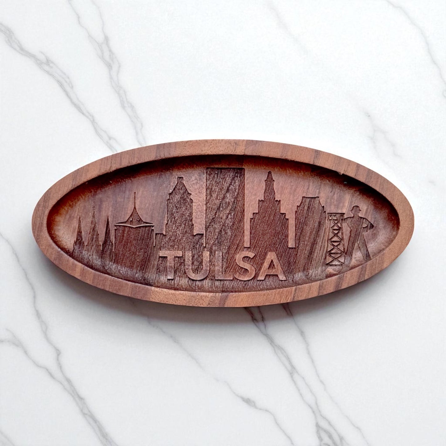 Top-down image of a walnut wood tray engraved with Tulsa skyline and Golden Driller, on white marble surface