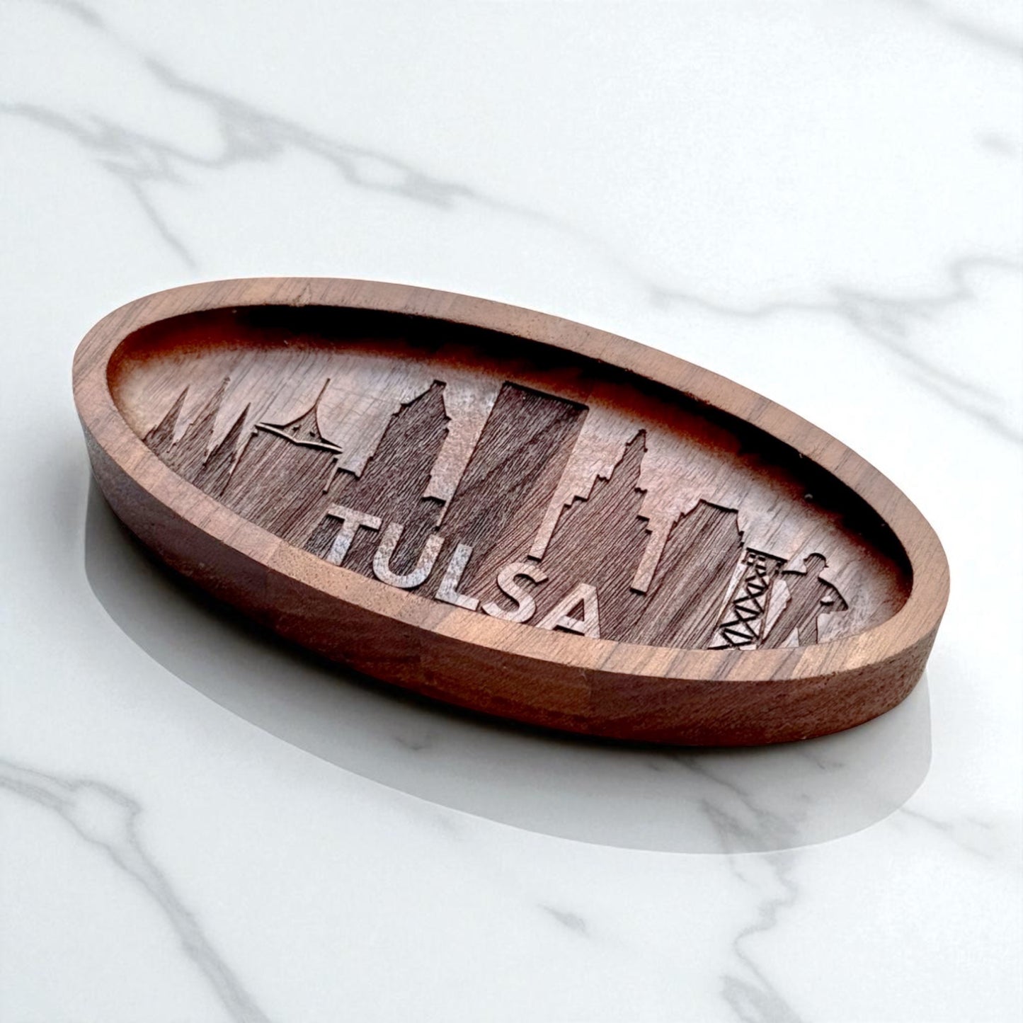 Angled view of engraved walnut wood ring tray with detailed Tulsa skyline, styled on light marble