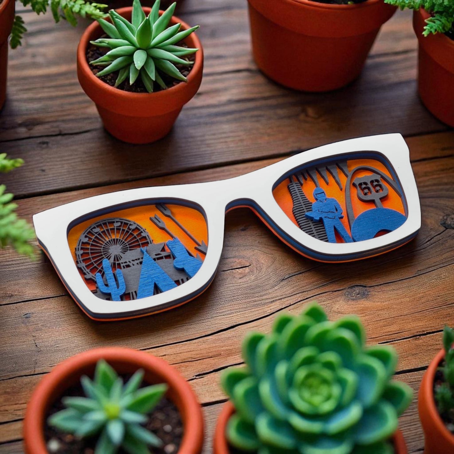 Angled shot of white wooden Route 66 sunglasses wall decor surrounded by succulents, highlighting the playful layered design of Route 66 icons like the Cadillac Ranch, Muffler Man, and Cloud Gate.