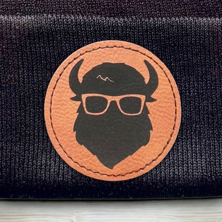 Detailed view of Curious Bison bison logo leatherette patch heat pressed onto black knit beanie
