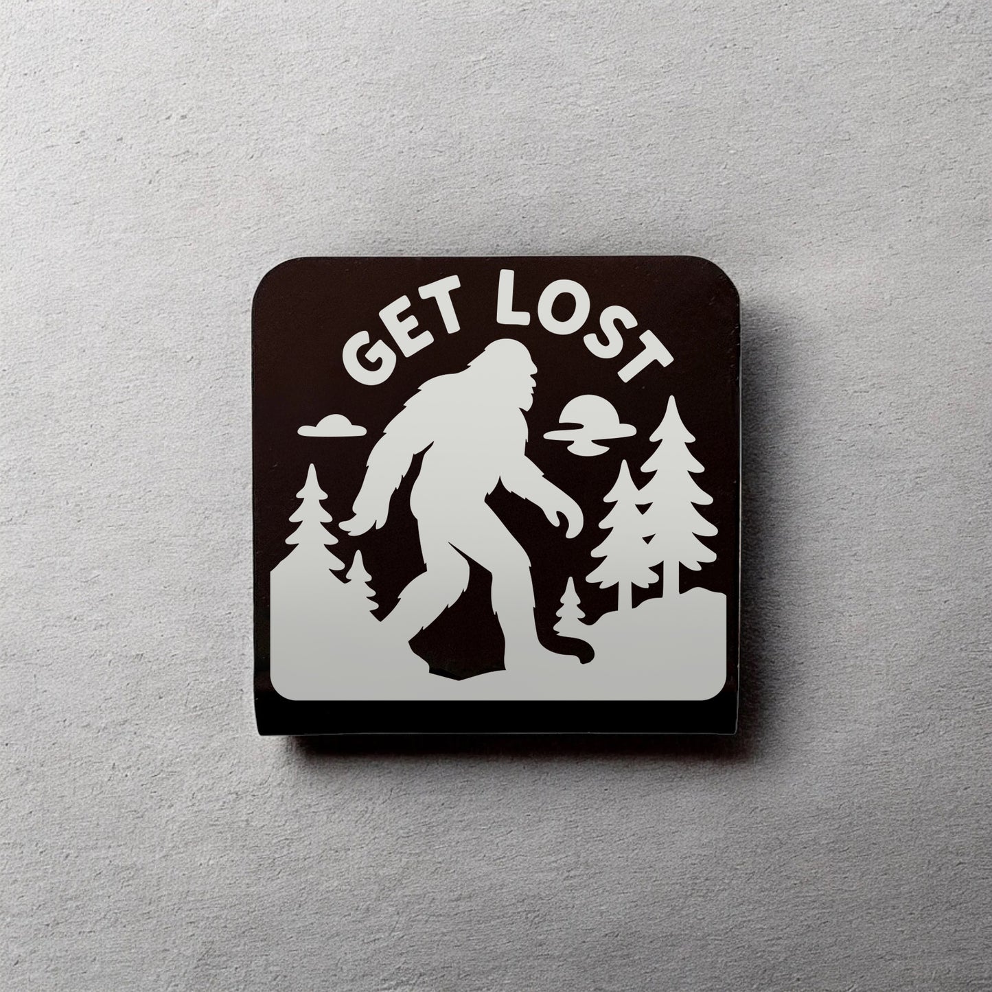 Get Lost Bigfoot aluminum hat clip displayed on wall showing Sasquatch outdoor design, novelty hat clip for outdoor lovers