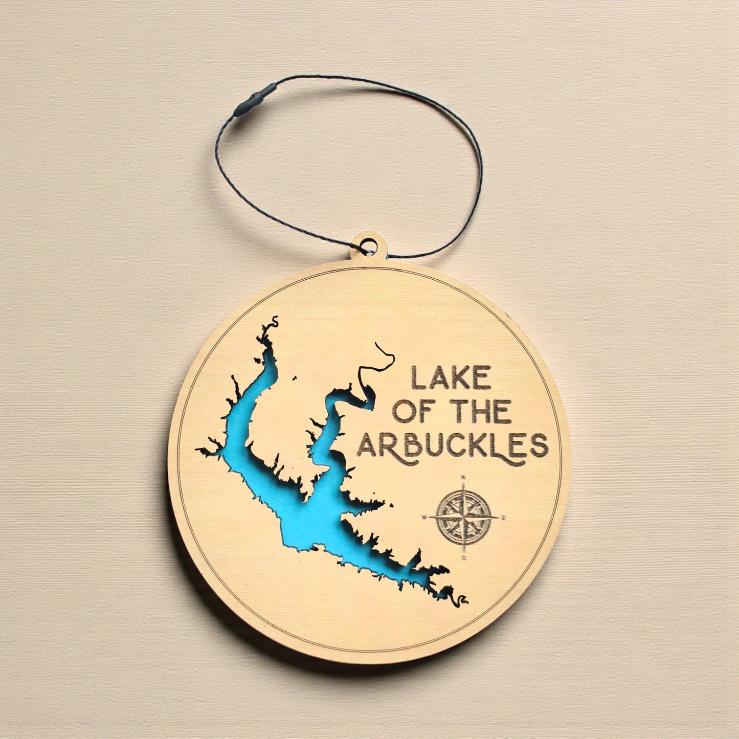 Lake of the Arbuckles wooden ornament hanging on evergreen tree with lights, layered wood lake ornament with engraved lake name and blue water layer