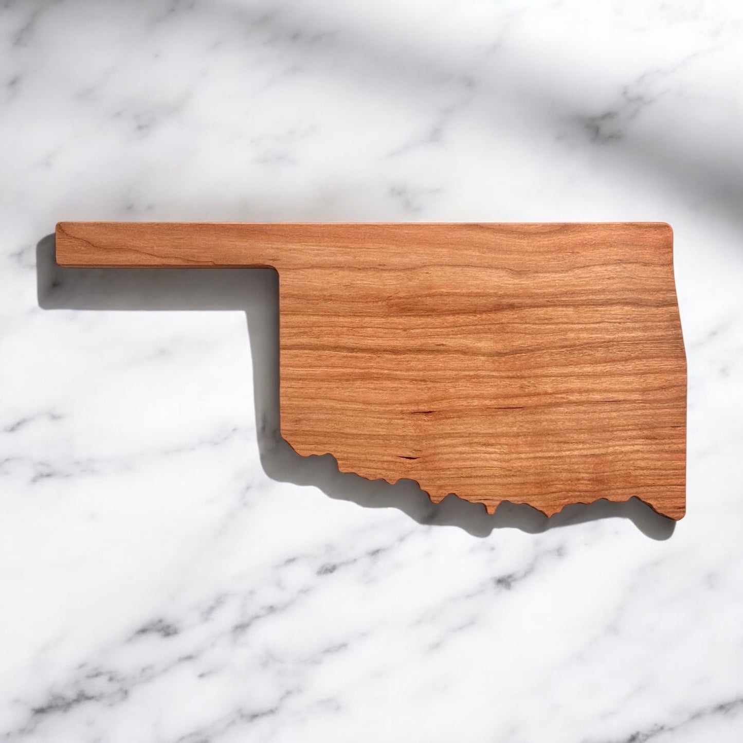 Minimalist Oklahoma state-shaped cherry wood charcuterie board on marble background, shown without engraving
