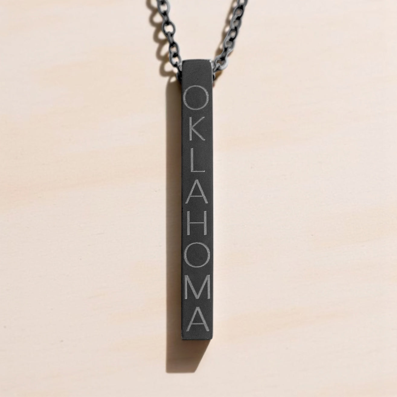 Vertical bar necklace in matte black with Oklahoma engraving on dark chain.