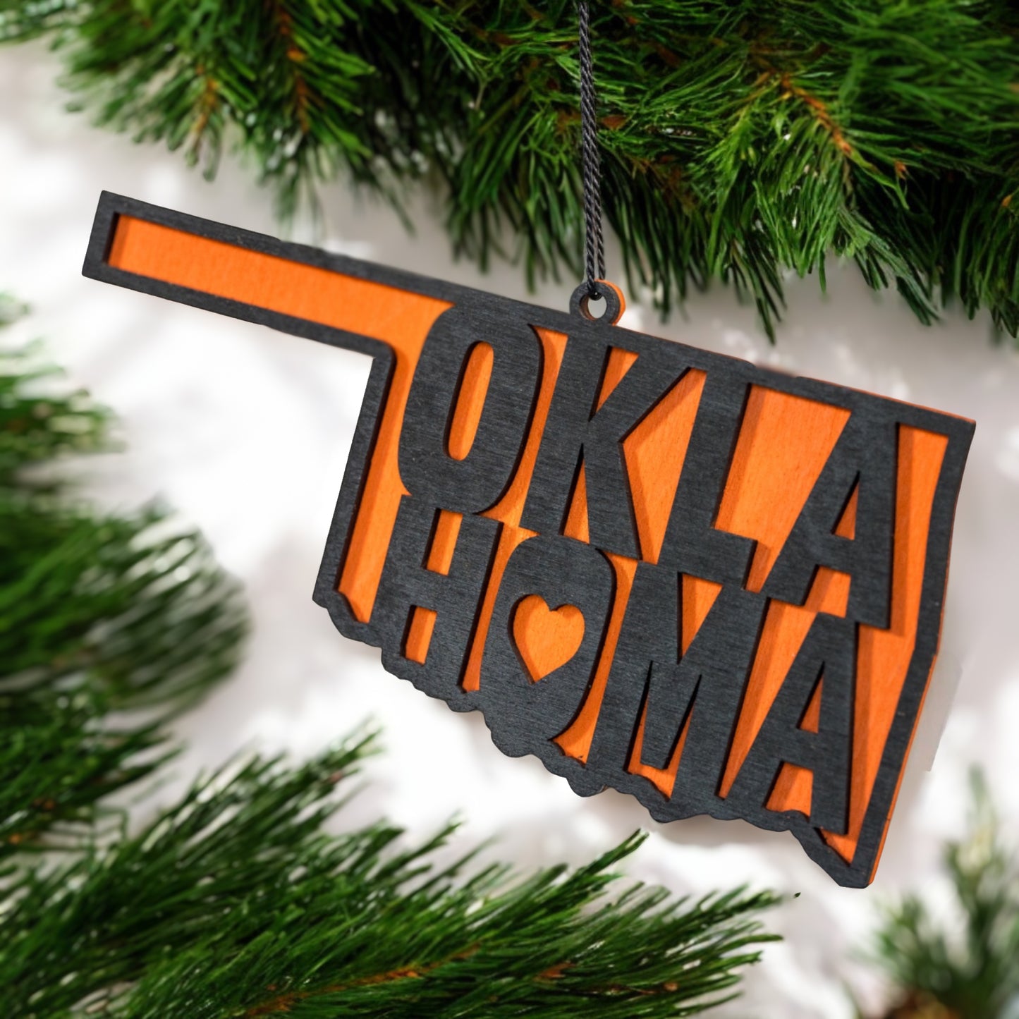 Oklahoma home wooden ornament hanging on evergreen tree, layered wood state shape ornament with orange backing used as Oklahoma Christmas decor