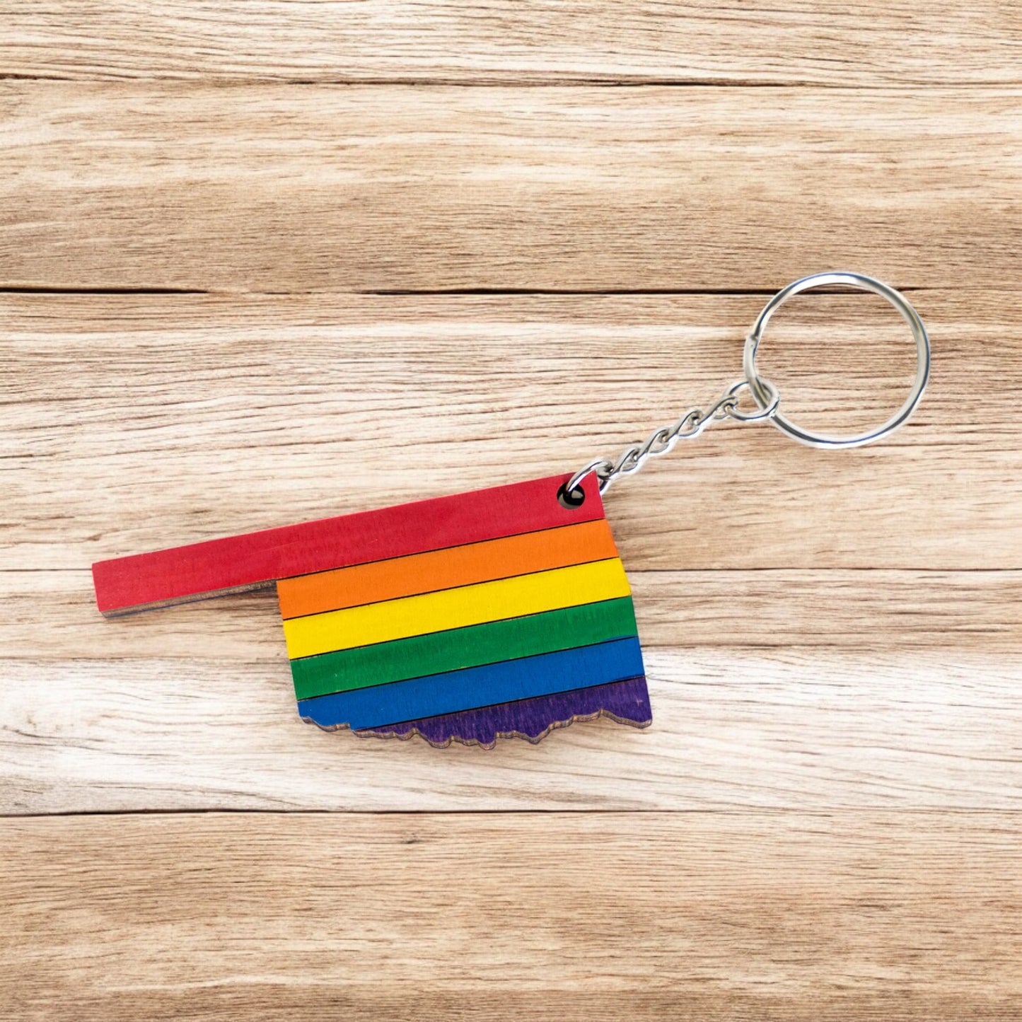 Flat lay of Oklahoma rainbow keychain on wood surface, layered wood pride keychain with Oklahoma state silhouette