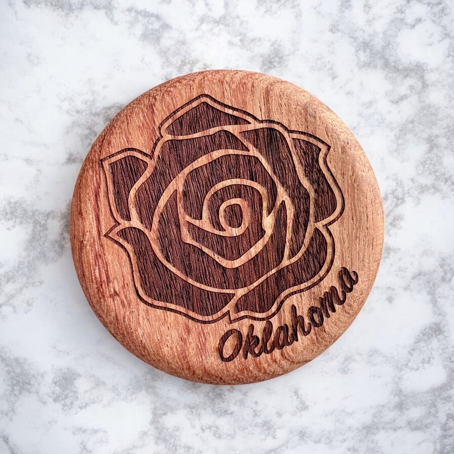 Close-up of round cherry wood bottle opener engraved with a detailed rose and Oklahoma lettering