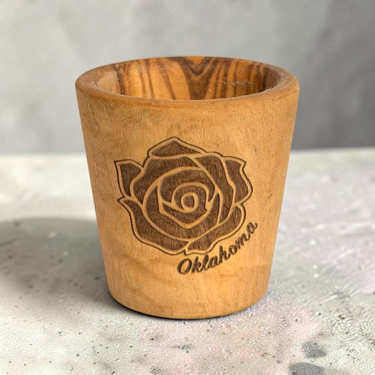 Laser engraved Oklahoma rose olive wood shot glass standing on a tabletop, natural wooden Oklahoma souvenir and gift with visible wood grain