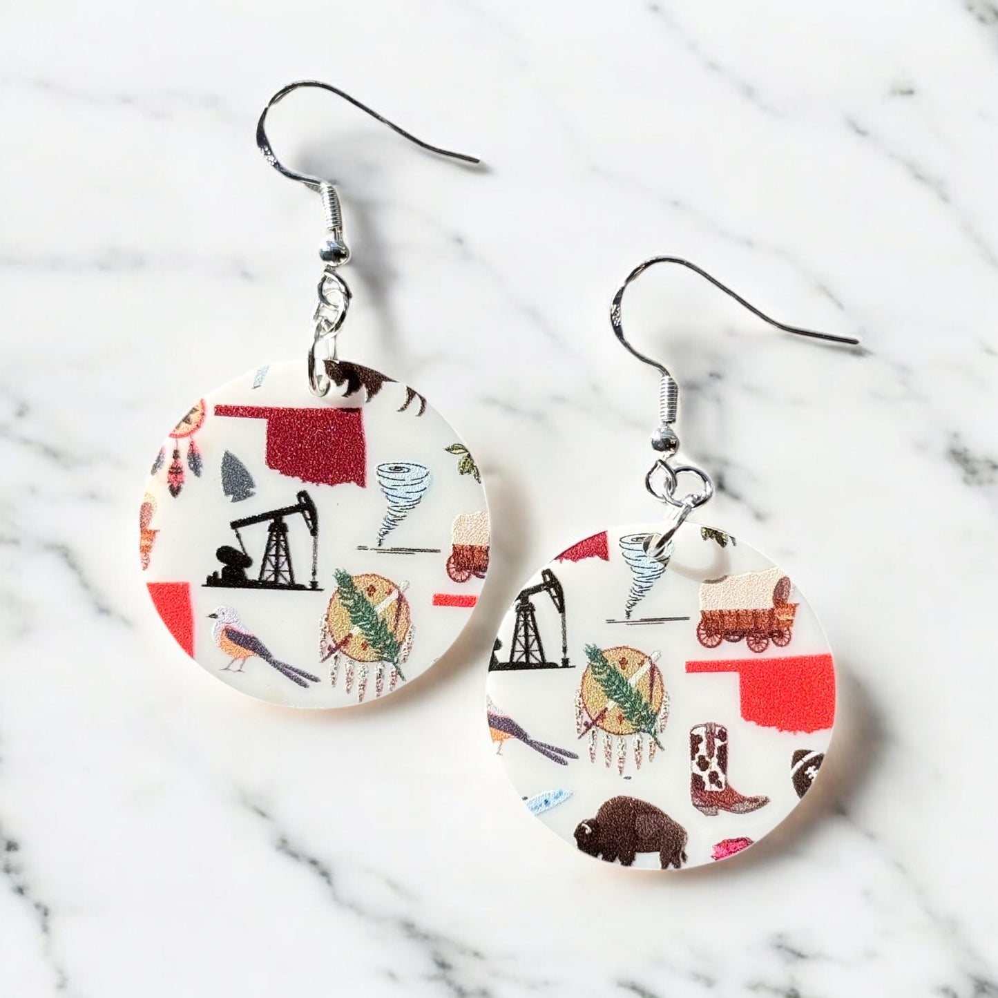 Pair of round acrylic Oklahoma symbol earrings with sterling silver ear hooks displayed on marble surface