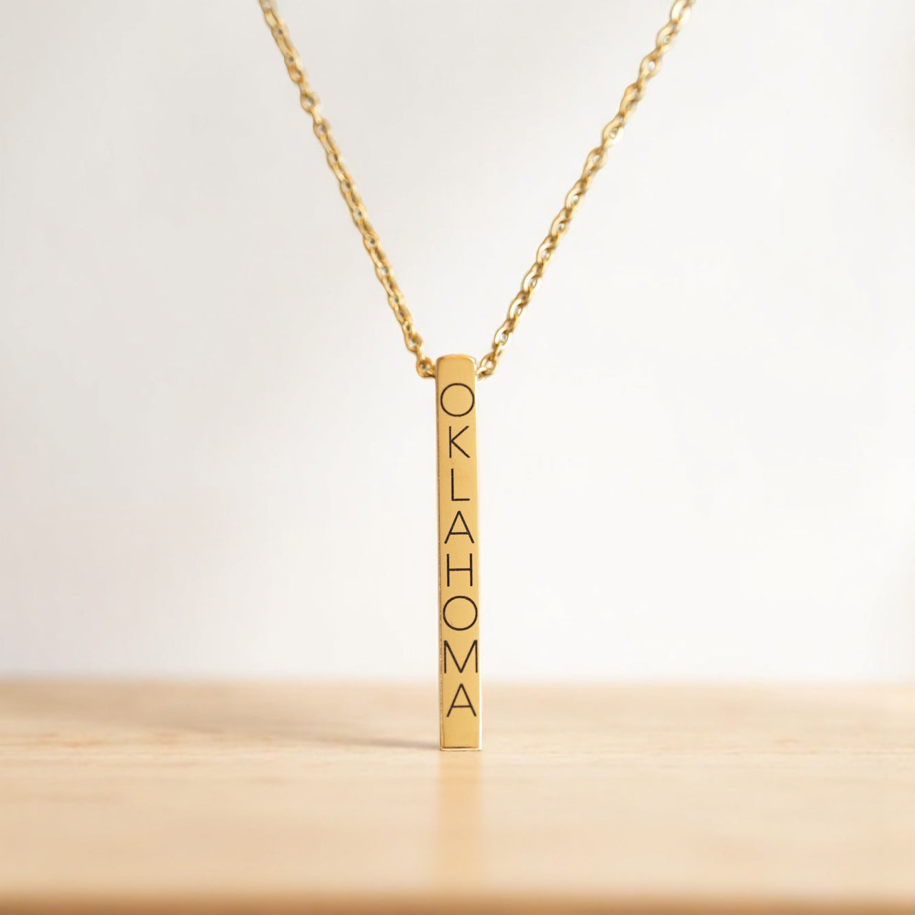 Close-up of gold Oklahoma vertical bar necklace with engraved letters on a gold chain.