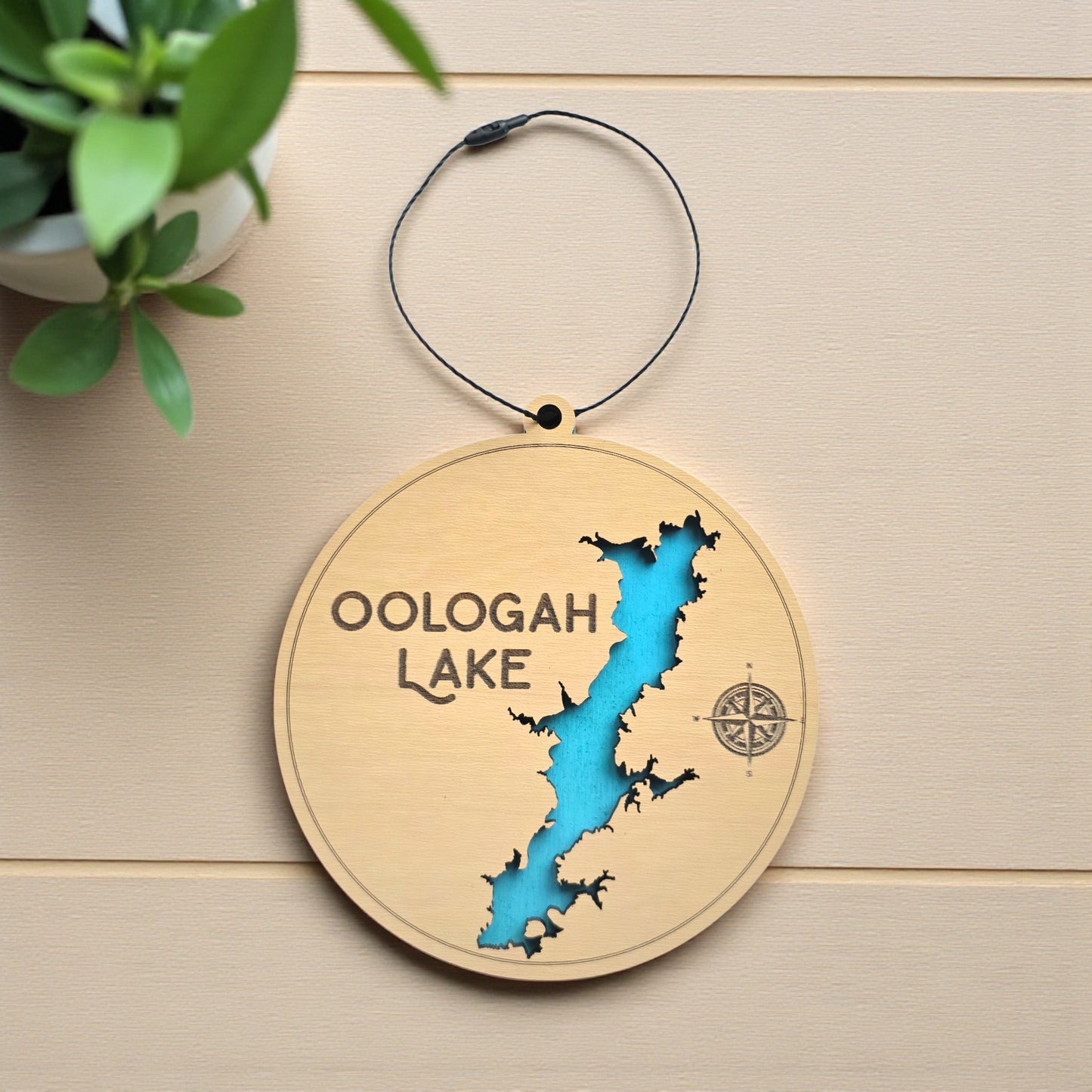 Flat lay of Oologah Lake layered wooden ornament showing engraved lake name, compass detail, and blue painted water layer beneath laser cut wood top