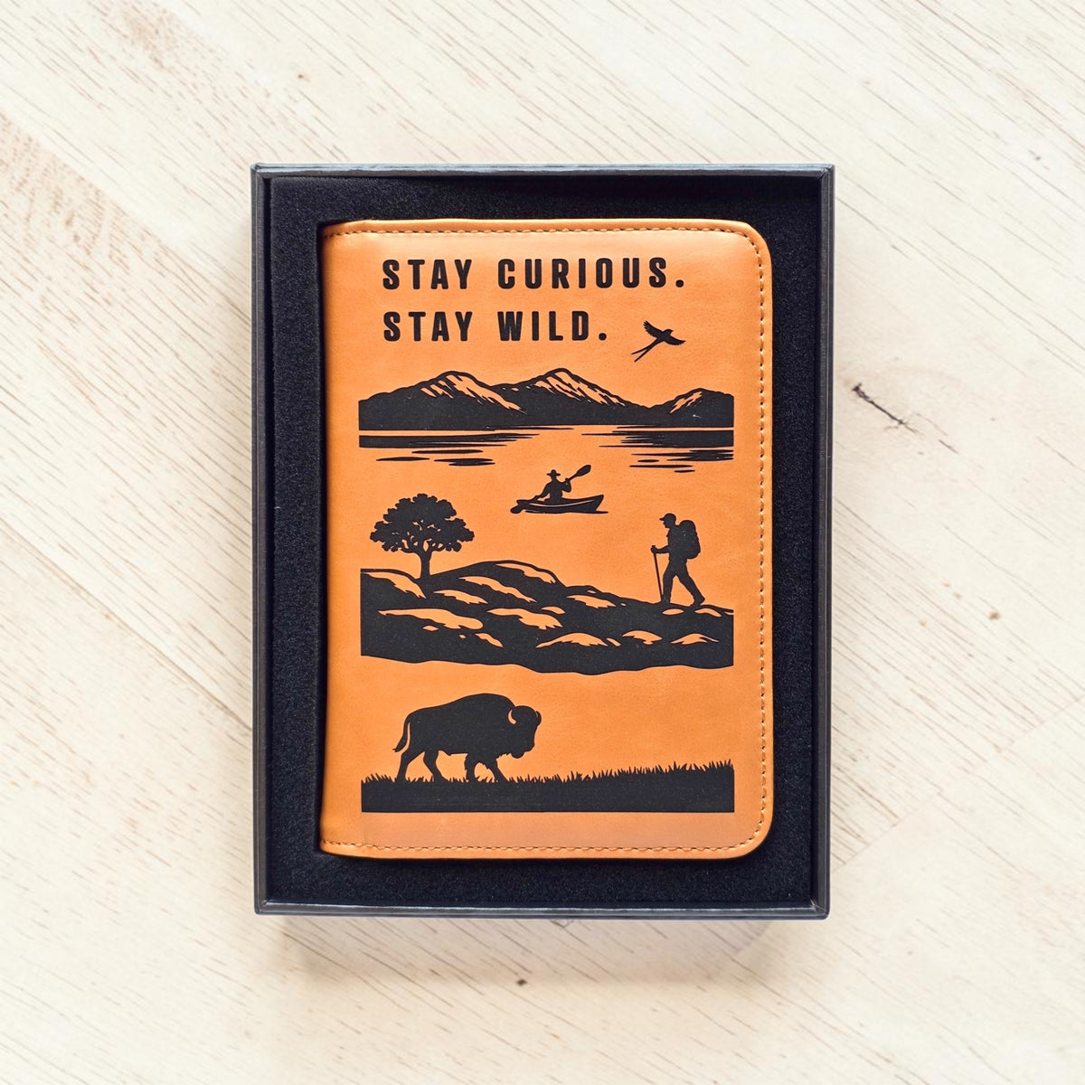 Adventure passport wallet displayed inside black gift box with engraved travel scene and Stay Curious Stay Wild message, ready to gift passport cover for travel lovers