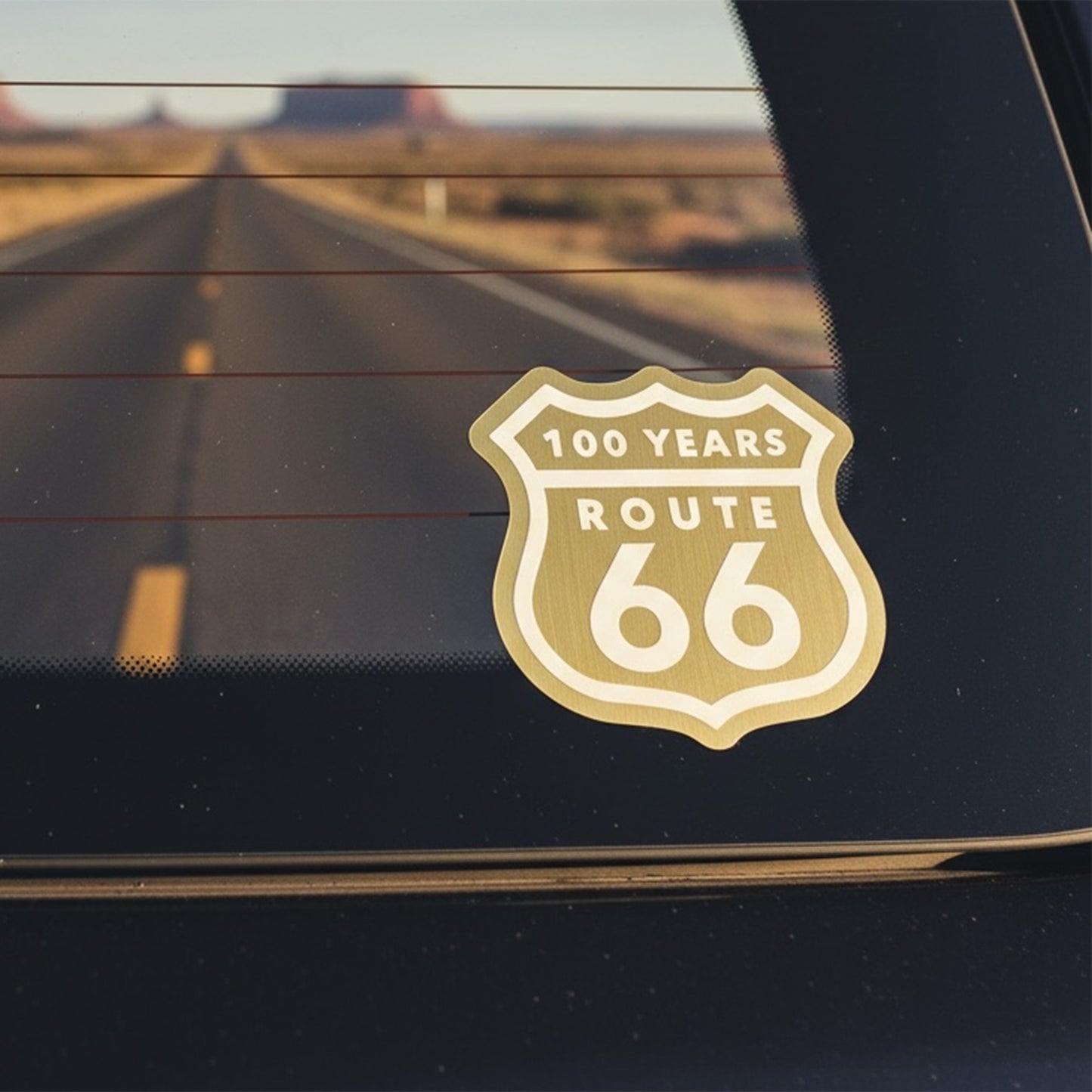 Route 66 centennial brushed gold vinyl sticker attached to rear car window during desert highway road trip, nostalgic Route 66 travel decal for Americana and road trip fans