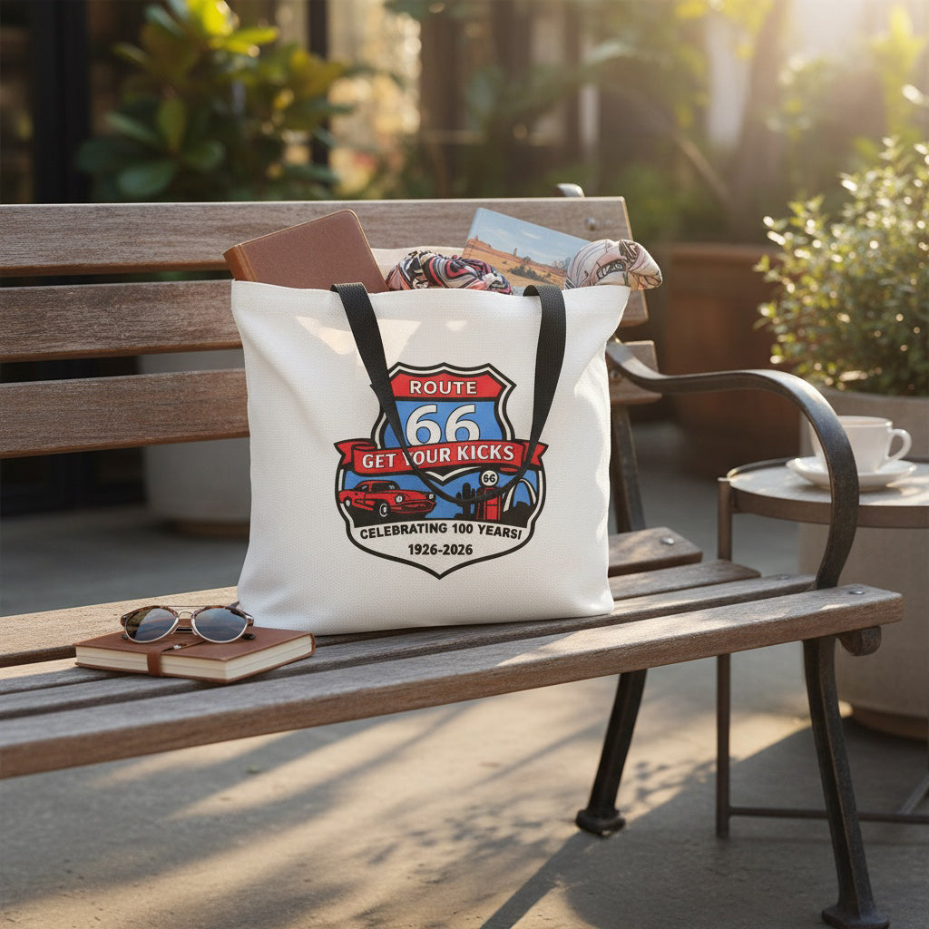 Lifestyle image of Route 66 Get Your Kicks tote bag sitting on a bench with travel accessories and postcards, designed as a functional Route 66 souvenir and Americana road trip bag
