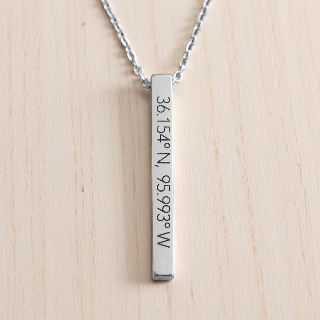 Sleek silver bar necklace with Tulsa coordinates 36.154°N, 95.993°W, illuminated by soft natural light.