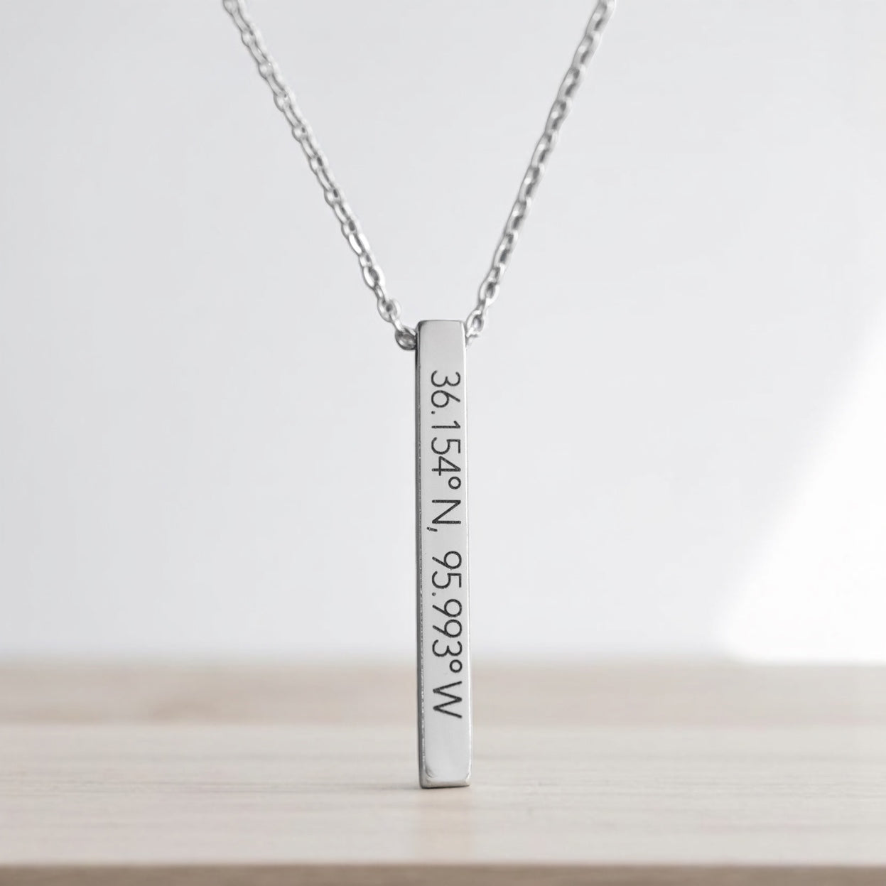 Minimalist silver Tulsa coordinates necklace featuring 36.154°N, 95.993°W, photographed on a pale wood background.