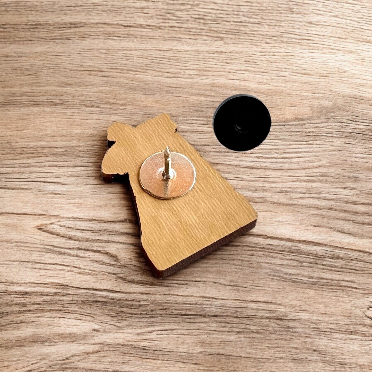 Back of Tulsa Driller wooden pin showing metal post and black rubber pin back, lightweight wood lapel pin for hats and jackets