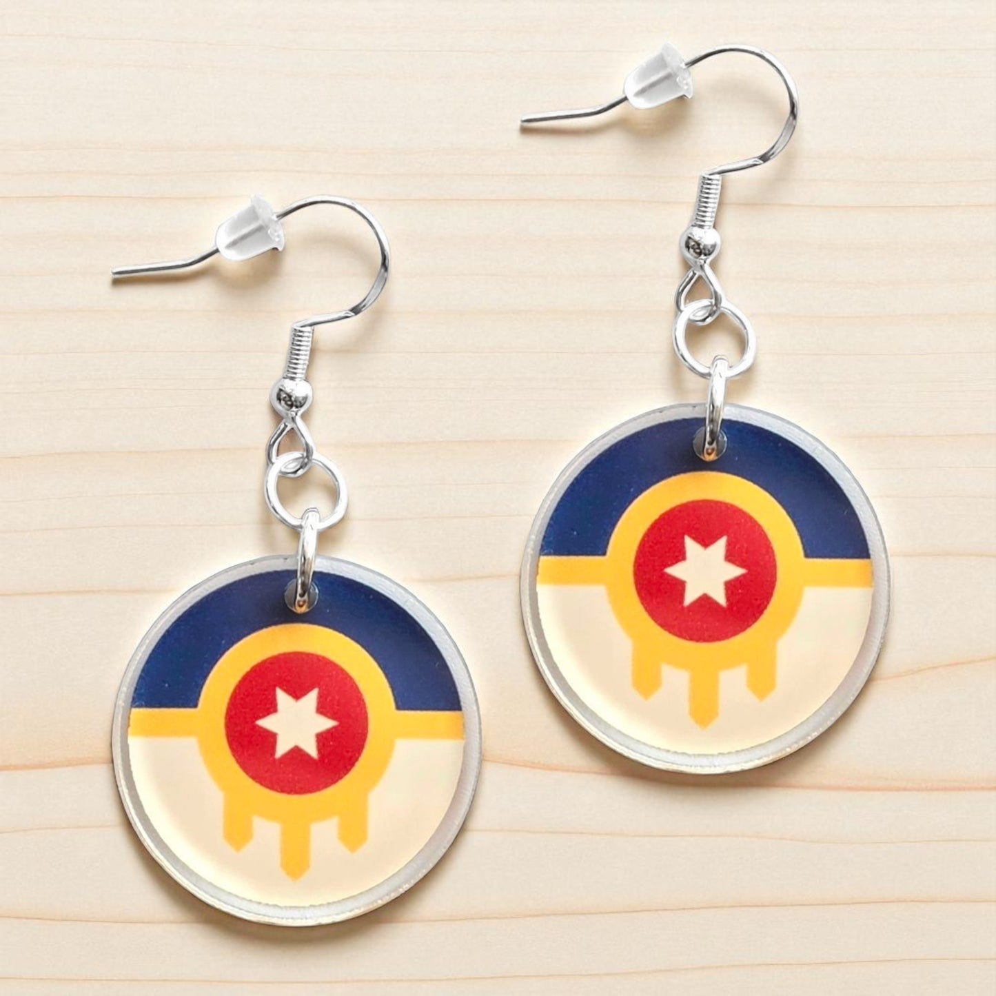 Pair of Tulsa flag acrylic earrings displayed on light wood surface, round printed acrylic earrings with city flag design and silver hooks