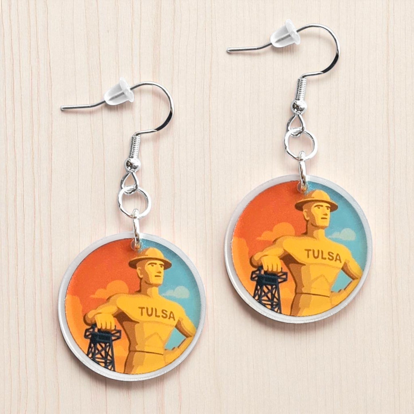 Pair of Tulsa Golden Driller acrylic earrings displayed on light wood surface, round printed acrylic earrings featuring Tulsa landmark design