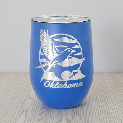 Blue 12oz wine tumbler with a laser etched Oklahoma scissortail flycatcher design, shown on a wood tabletop with a neutral background. This insulated stemless wine tumbler is a functional Oklahoma souvenir, ideal for wine and mixed drinks, and commonly purchased as a gift by Oklahoma locals and Route 66 travelers.