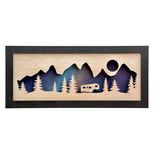 Layered wood wall decor featuring a 5th wheel trailer among pine trees and mountain peaks under a cosmic night sky