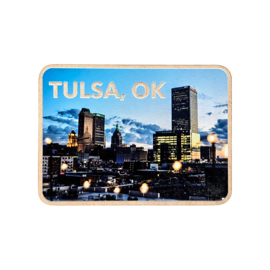 Downtown Tulsa night skyline wood photo magnet isolated on a white background. The magnet features lit city buildings and string lights against a dramatic evening sky with the text “TULSA, OK” at the top.
