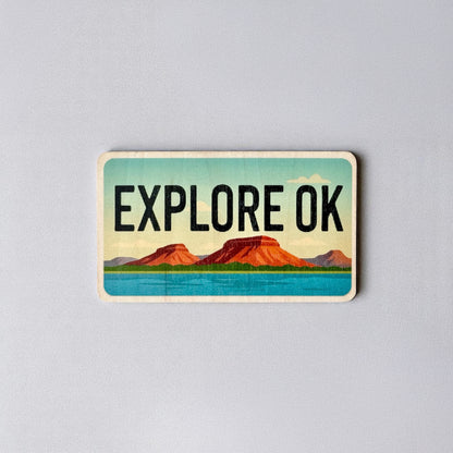 Vintage-style wood sticker that says “Explore OK” with red mesas and bright blue water, inspired by Oklahoma’s natural beauty.