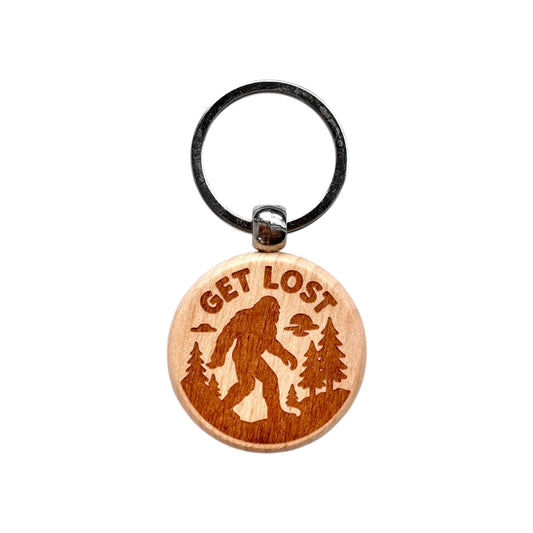 Laser-engraved round wooden keychain featuring a Bigfoot silhouette and the phrase “GET LOST” on a white background