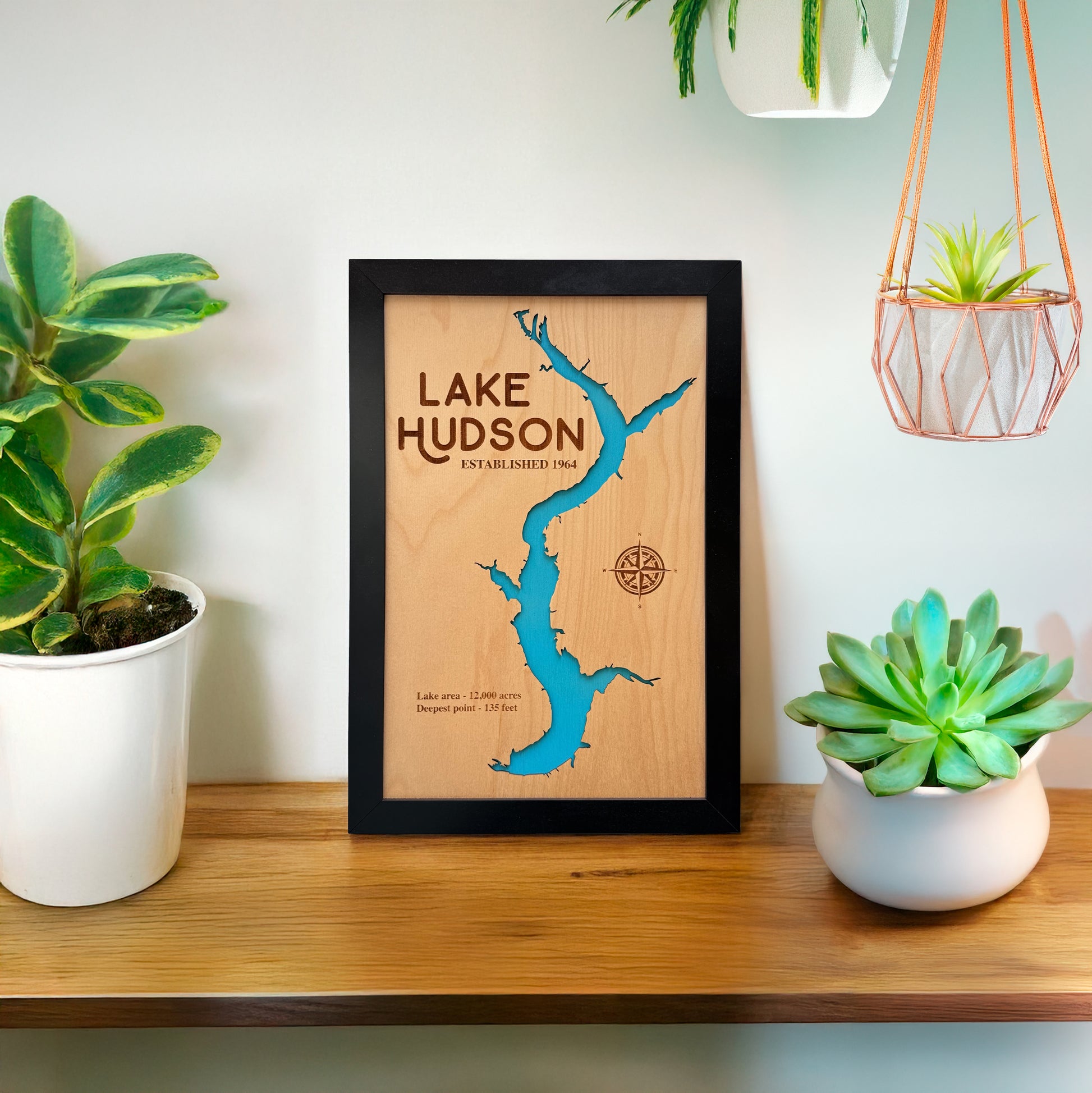 Wooden map of Lake Hudson sitting on a shelf with plants around it