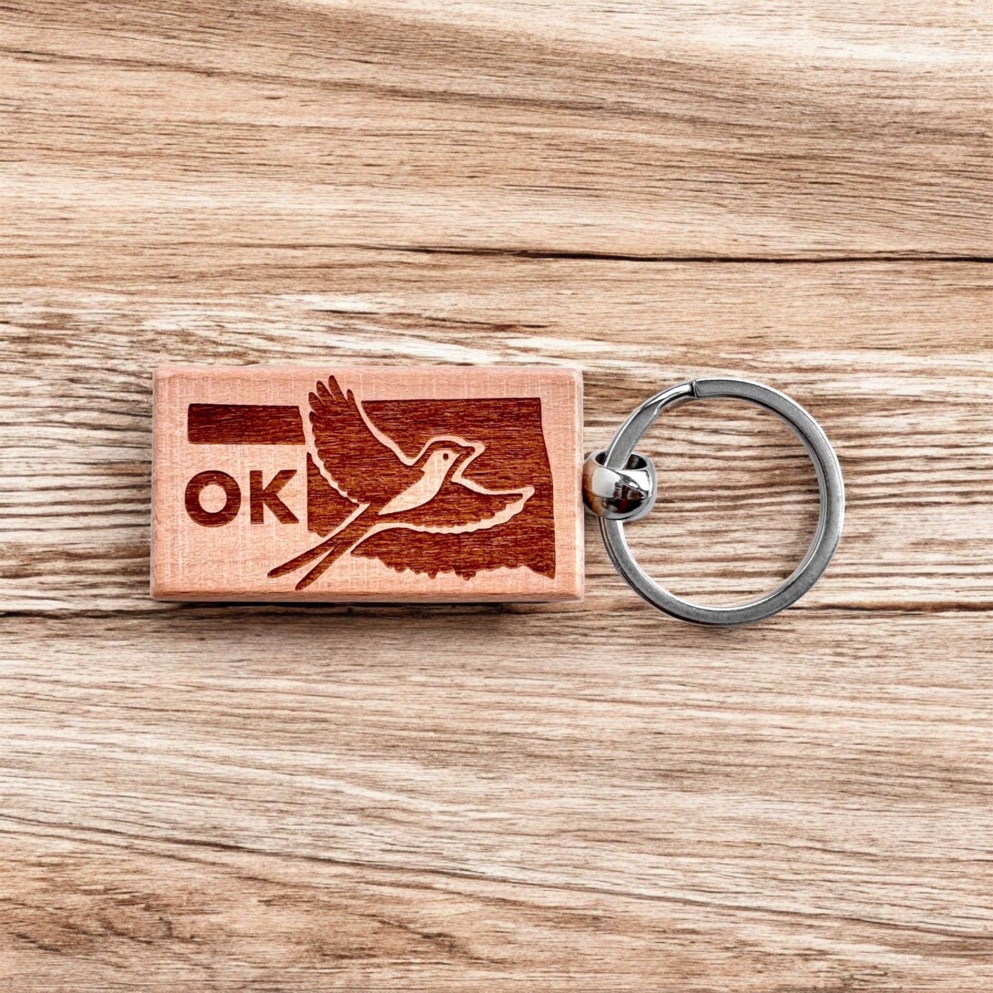 Wooden Oklahoma keychain with a laser-engraved Scissor-tailed Flycatcher in flight over the state outline, shown on a rustic wood background.