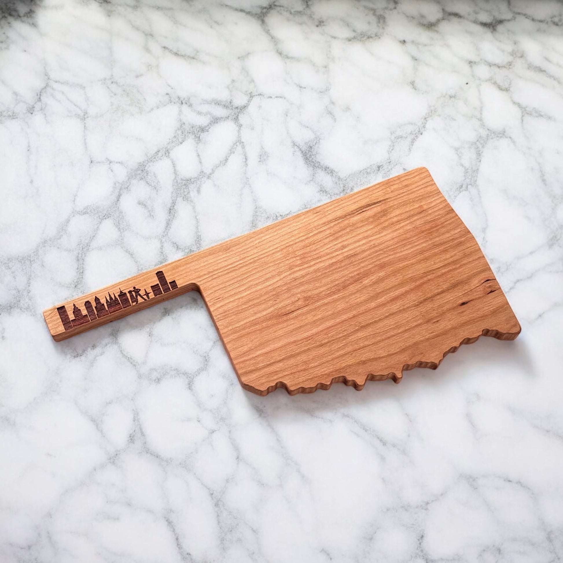 Oklahoma cherry wood charcuterie board featuring laser-engraved Tulsa skyline, shown at an angle on marble.