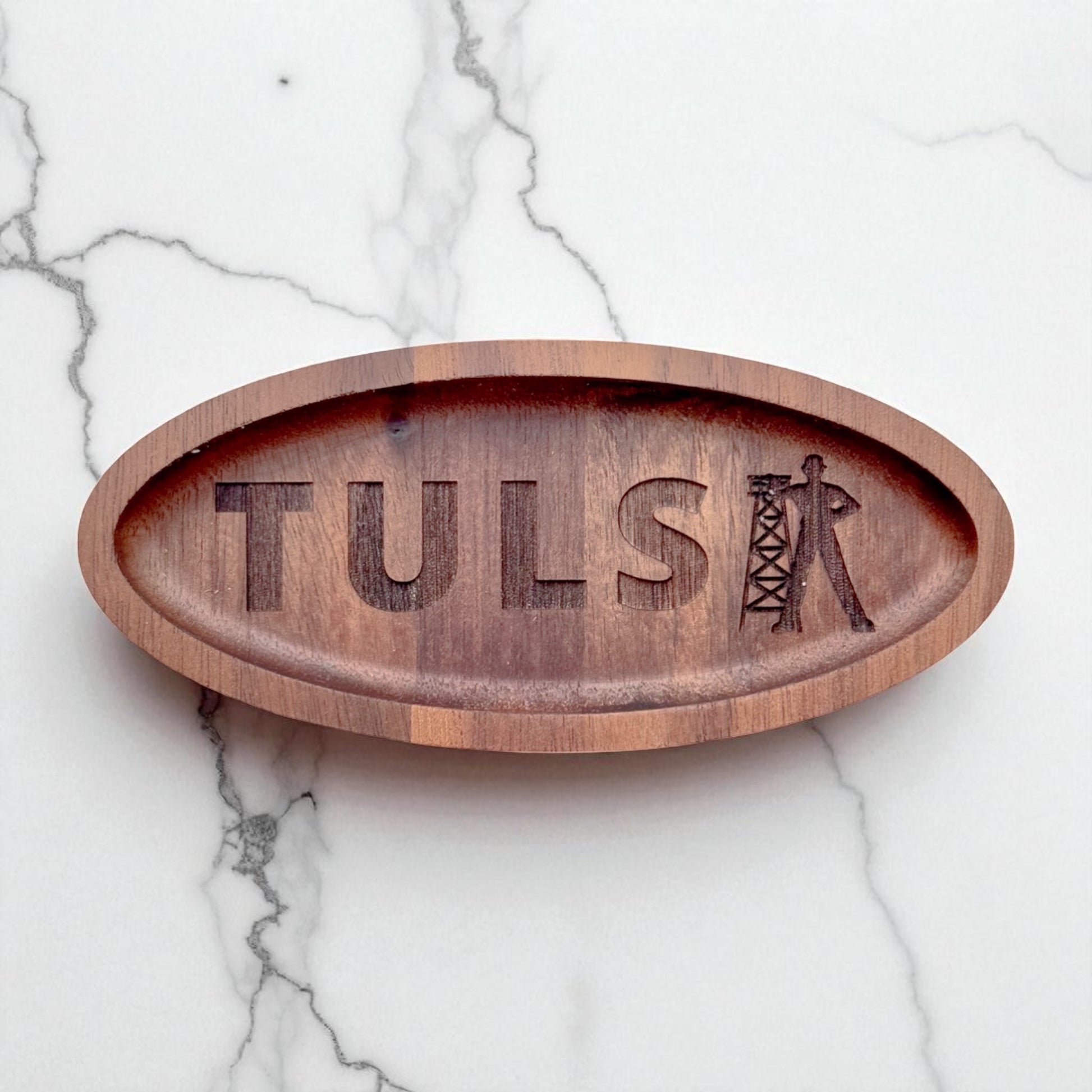 Flat-lay of a laser-engraved walnut ring tray with Tulsa and oil driller design, styled on white marble