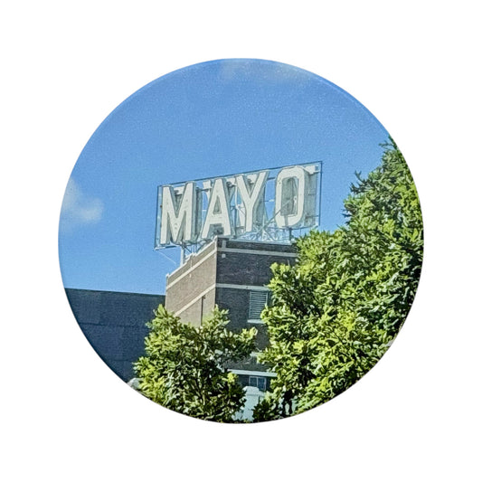Round Tulsa-themed ceramic coaster featuring the Mayo Hotel rooftop sign, set against a bright blue sky and vibrant green foliage, isolated on white