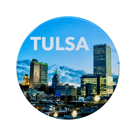 Round ceramic coaster with a vivid evening skyline of Tulsa, Oklahoma, with “TULSA” in bold white text, isolated on white background