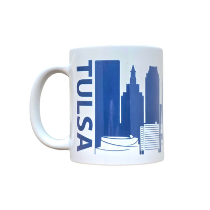 White ceramic mug featuring navy Tulsa skyline silhouette with Golden Driller and city buildings.