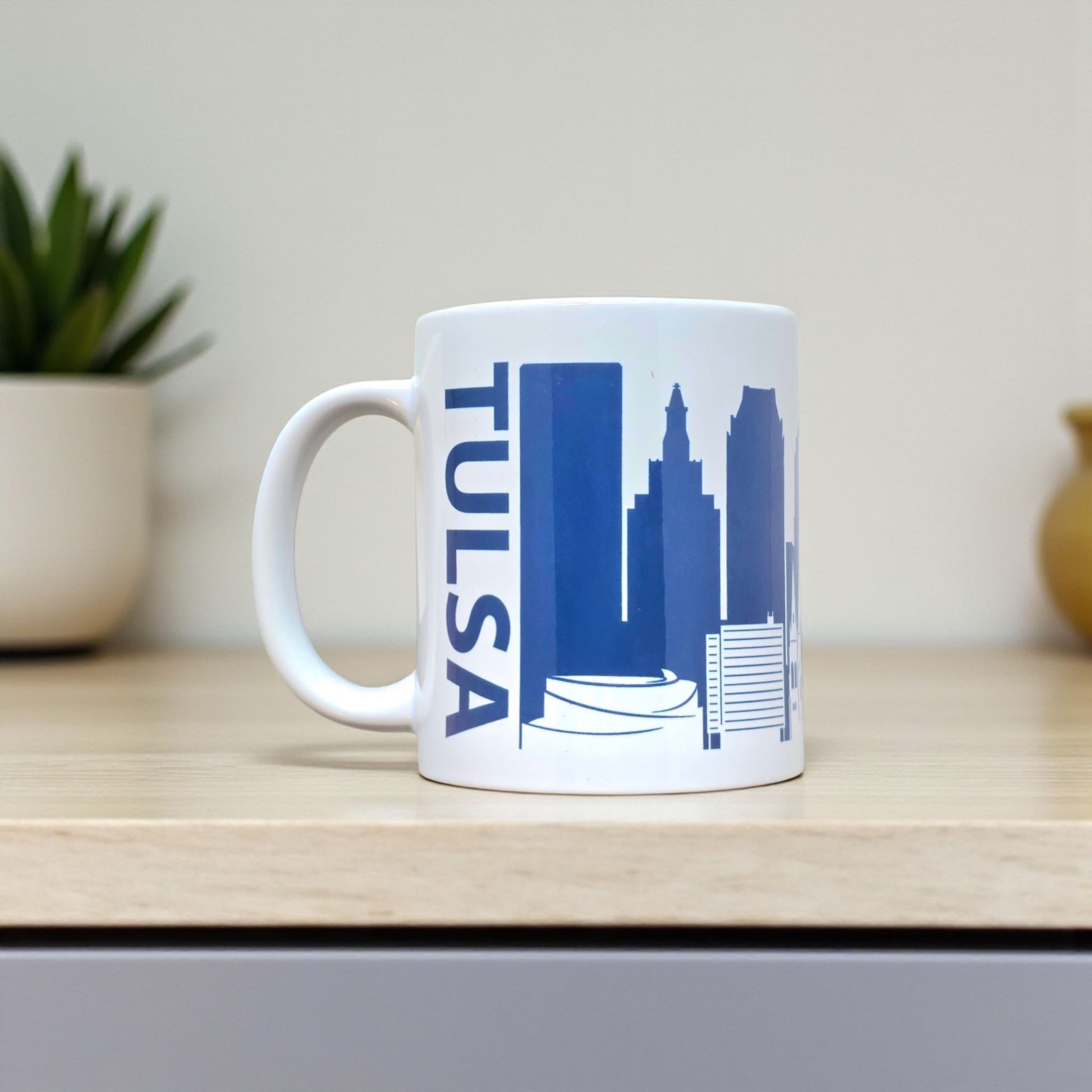 Tulsa skyline coffee mug with navy design and bold “TULSA” text, styled on tabletop.
