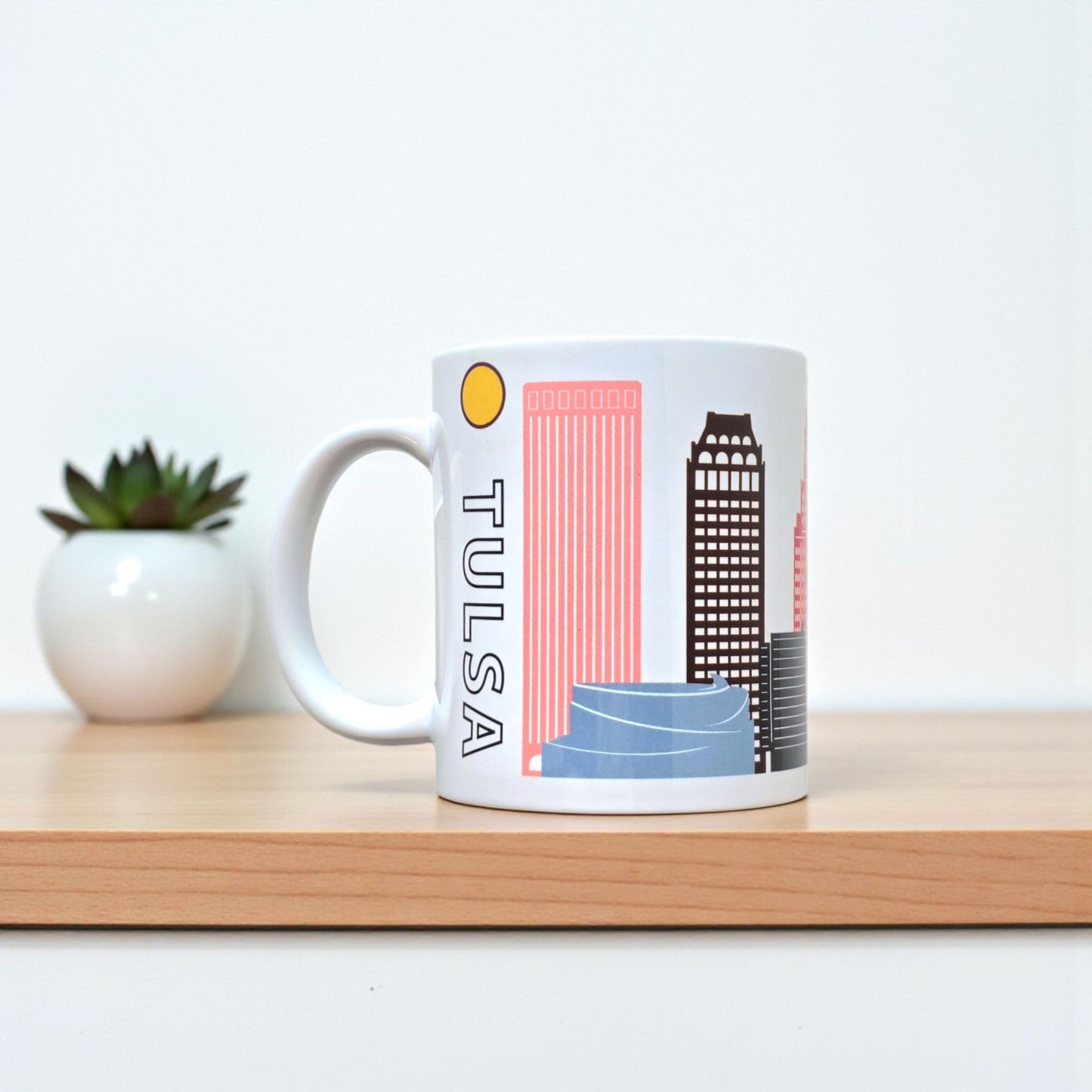 Tulsa rainbow skyline coffee mug displayed on desk with plant in background.