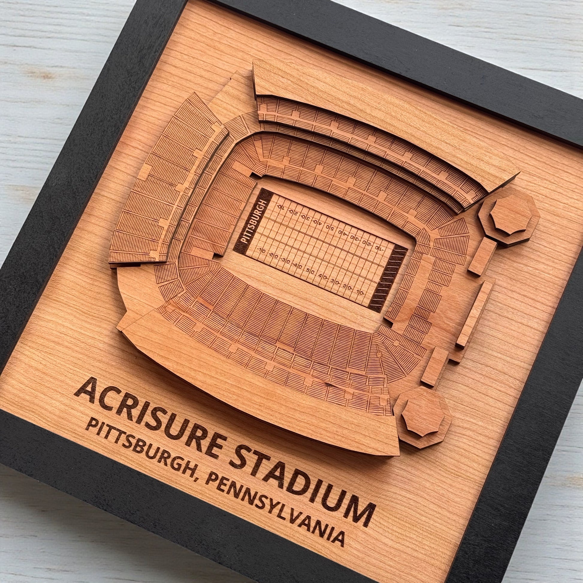 Angled view of Acrisure Stadium layered wooden wall art in black frame, engraved Pittsburgh football stadium map for office or home decor