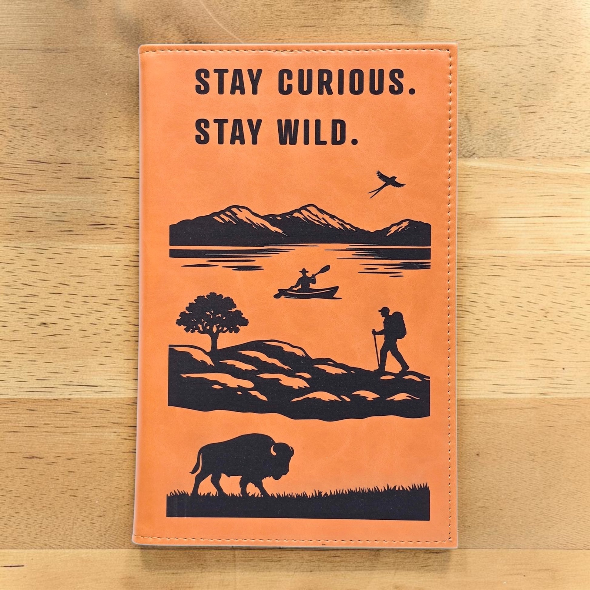 Adventure journal with Stay Curious Stay Wild quote on tan leatherette cover featuring mountain lake kayak hiker bird and bison artwork, travel notebook gift for hikers campers and road trip lovers in the USA