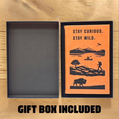 Open gift box showing Stay Curious Stay Wild adventure notebook with tan cover and outdoor art, thoughtful gift for travel lovers and road trip souvenir shoppers